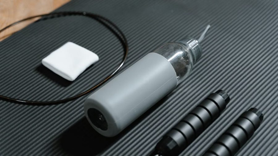 Gray water bottle and jump rope on textured black yoga mat. Indoor workout essentials.